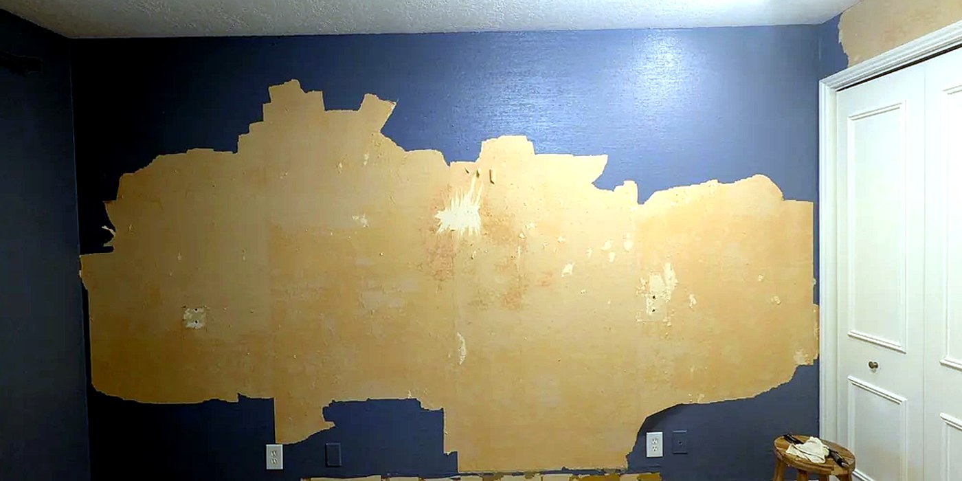 Large wall with torn drywall paper after adhesive removal