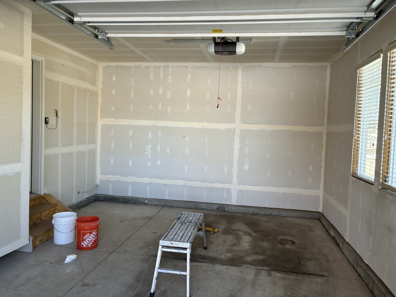 Garage during wall prep, wide view of mudded wall and ceiling seams over bare concrete