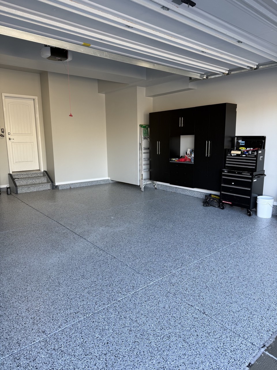 Finished garage with smooth painted drywall, base trim, grey flake epoxy floor, and wall cabinets